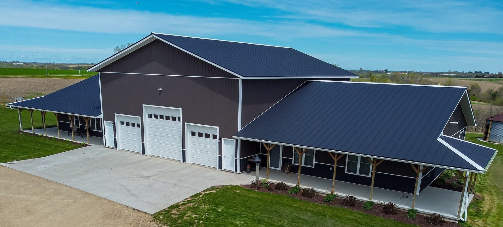 A finished barndominium with a wraparound porch and three garage doors